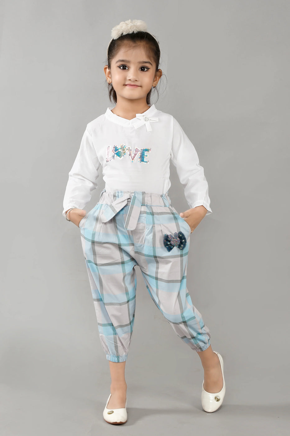Child wearing a white shirt with 'LOVE' text and plaid pants on a gray background