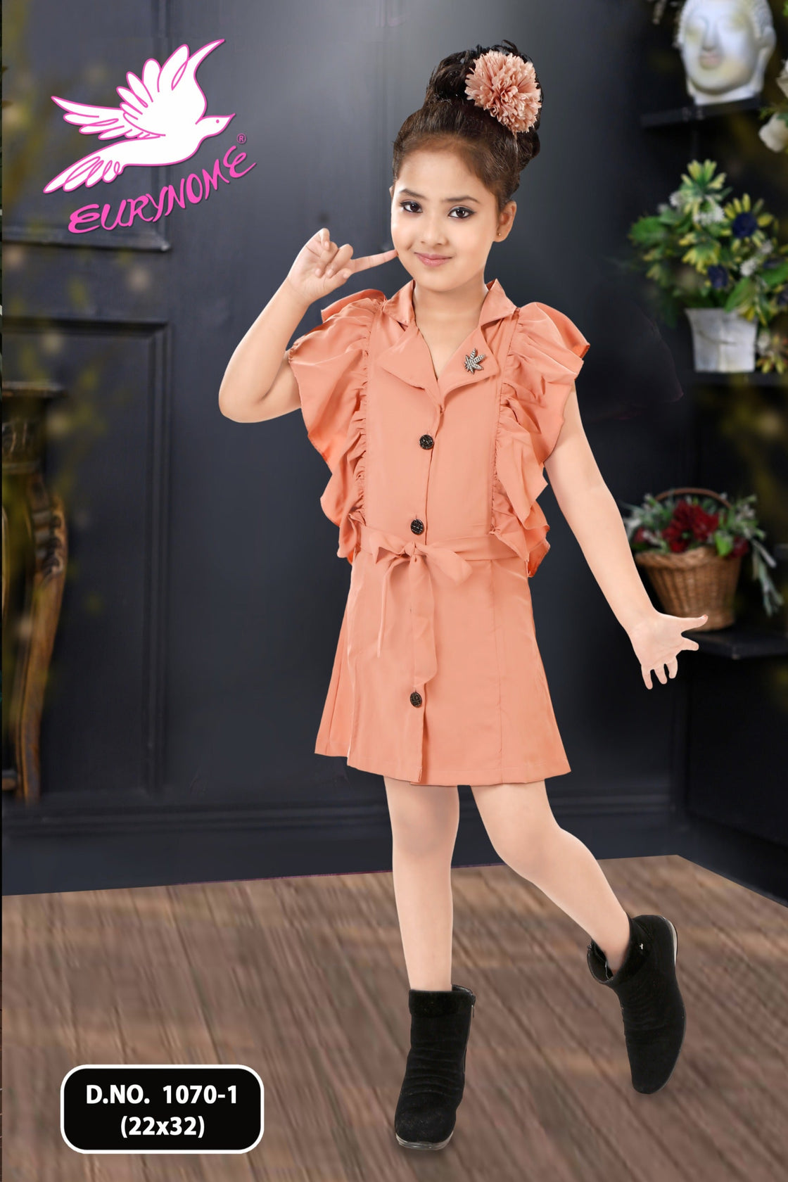 Young girl in a peach dress posing indoors with a brand logo in the background