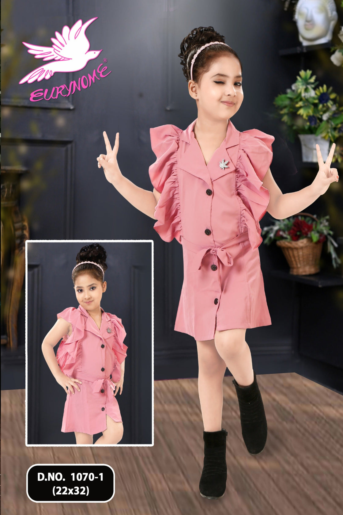 Young girl in a pink dress with ruffled details, standing indoors with a dark wall and plants in the background.