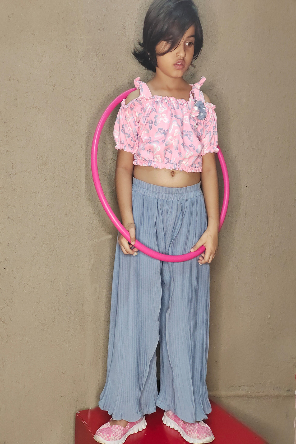 Young girl holding a pink hula hoop against a plain background